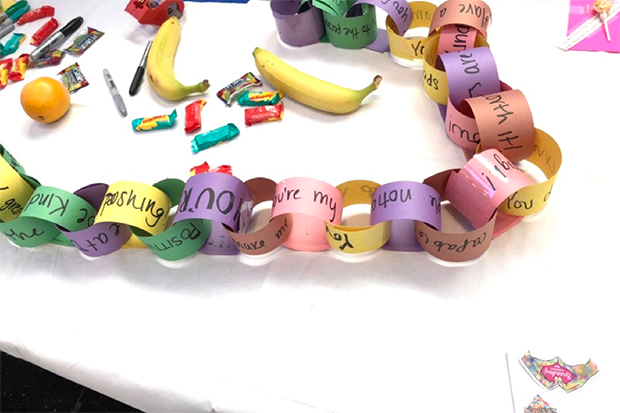 A paper chain created with notes on the kindest thing someone has done for you lays on a table with fruit and candy.
